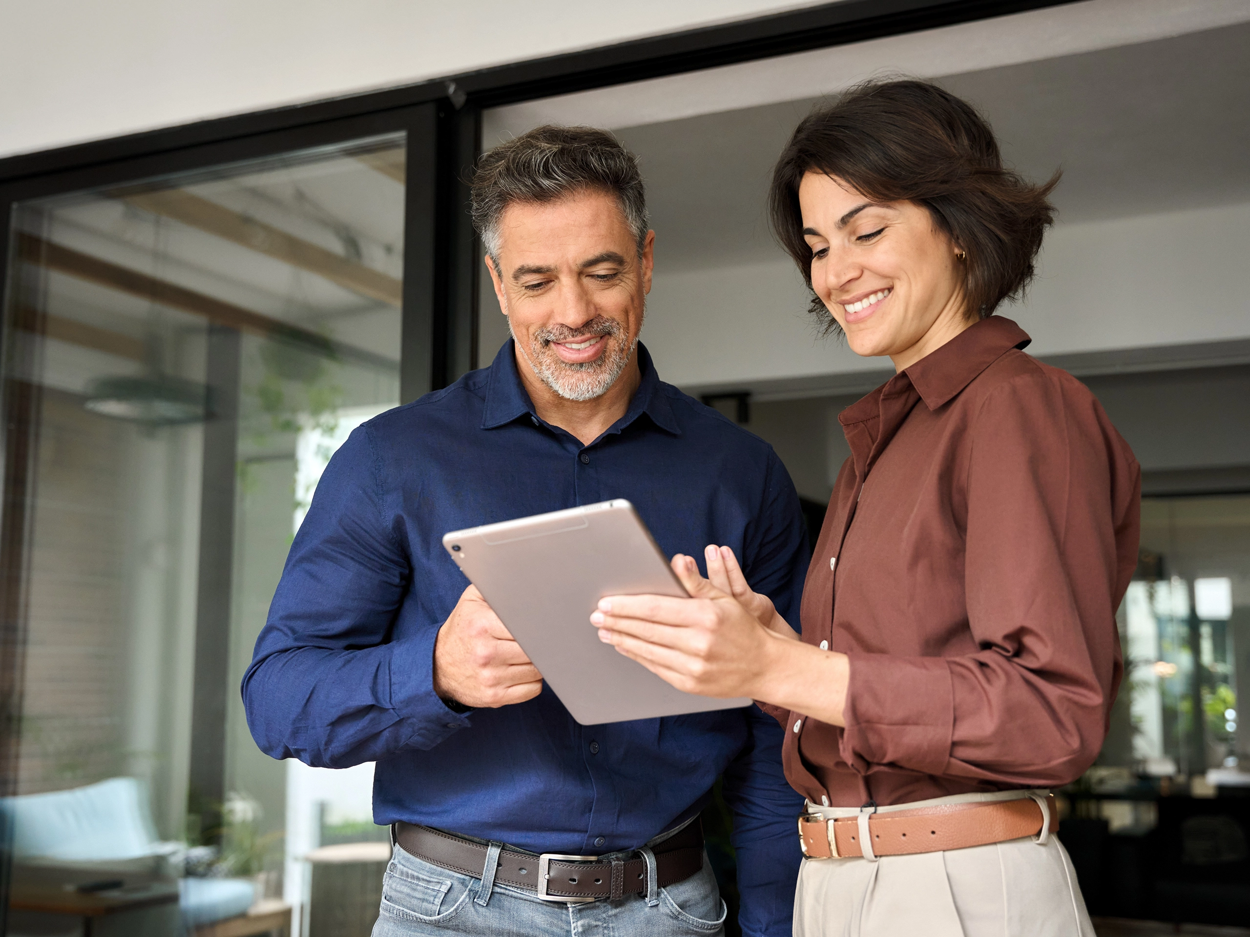 Professional business people, two happy busy business man and woman executives partners team working together standing in office using digital tablet in corporate cooperation on company project
