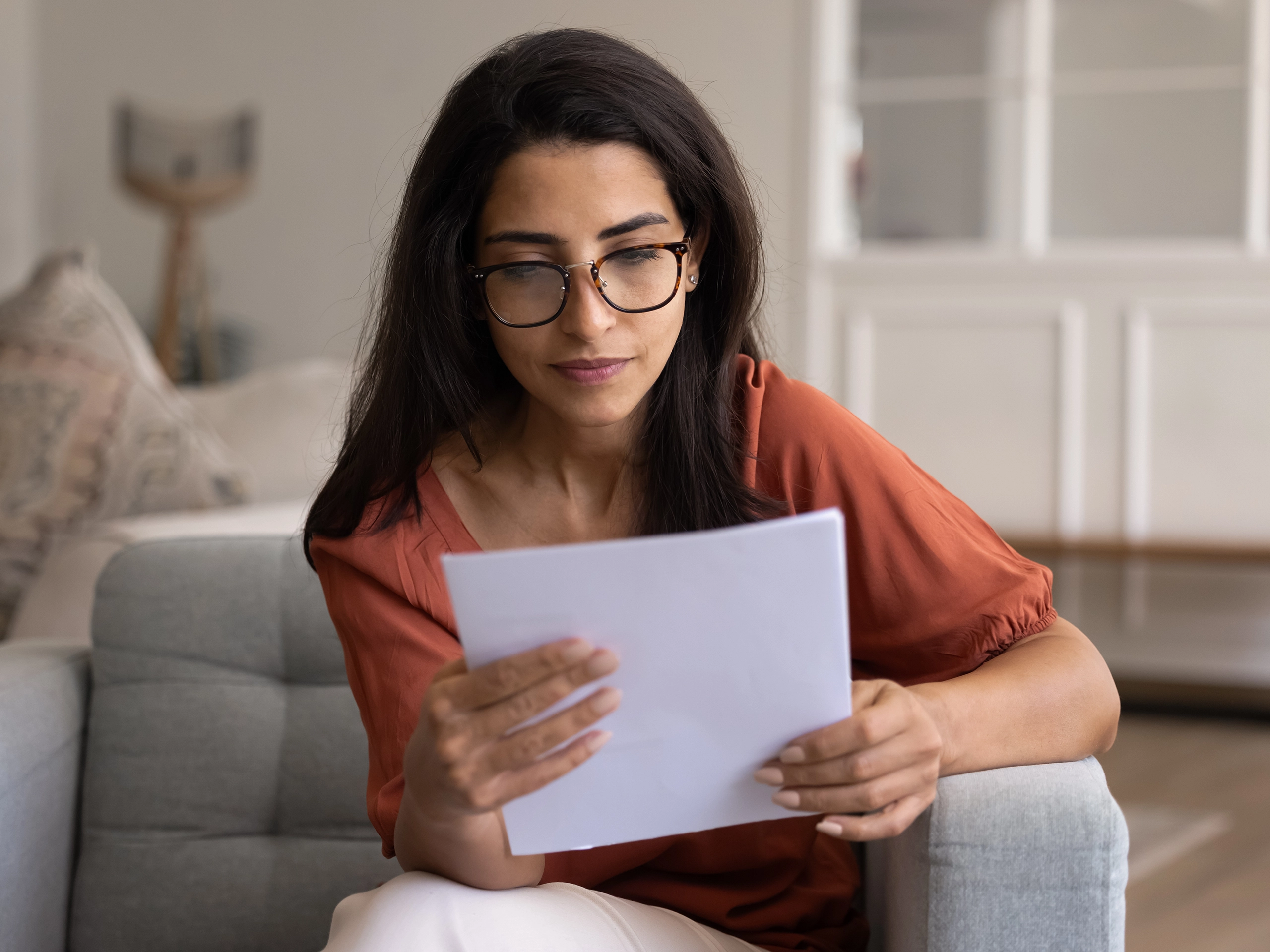 Focused smart Hispanic homeowner woman in glasses checking legal document at home
